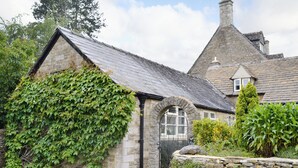 A stone cottage with a steeply pitched roof, a small arched entrance, and a stone wall with a yellow fire hydrant. - 1 bedroom accommodation in Ampney Crucis, near Cirencester (Ampney Crucis, near Cirencester)