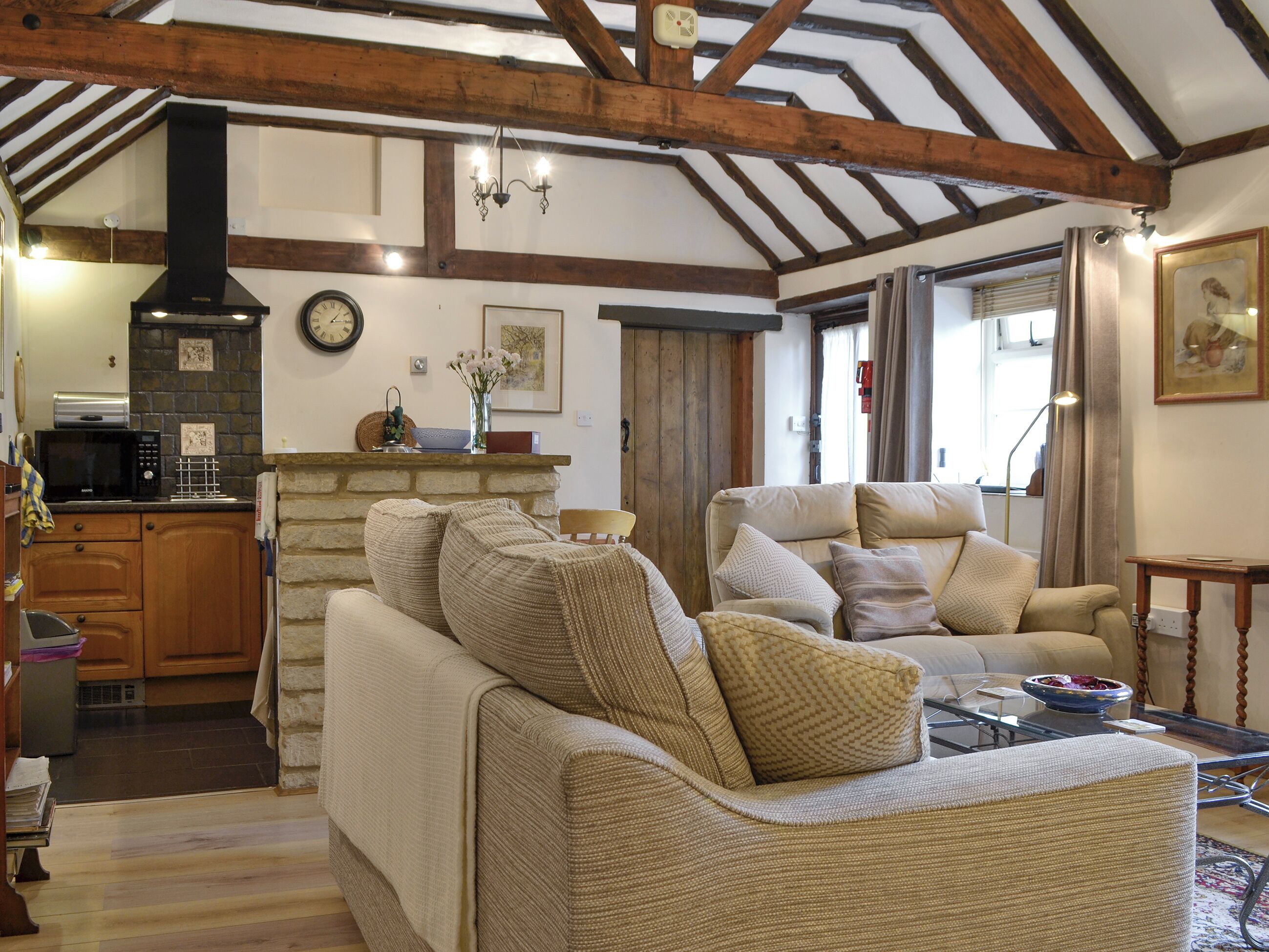 A cozy living room with a fireplace, wooden beams, a kitchen area, and comfortable seating.