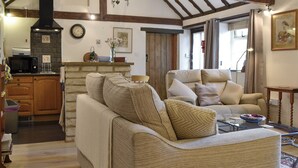 A cozy living room with a fireplace, wooden beams, a kitchen area, and comfortable seating. - 1 bedroom accommodation in Ampney Crucis, near Cirencester (Ampney Crucis, near Cirencester)