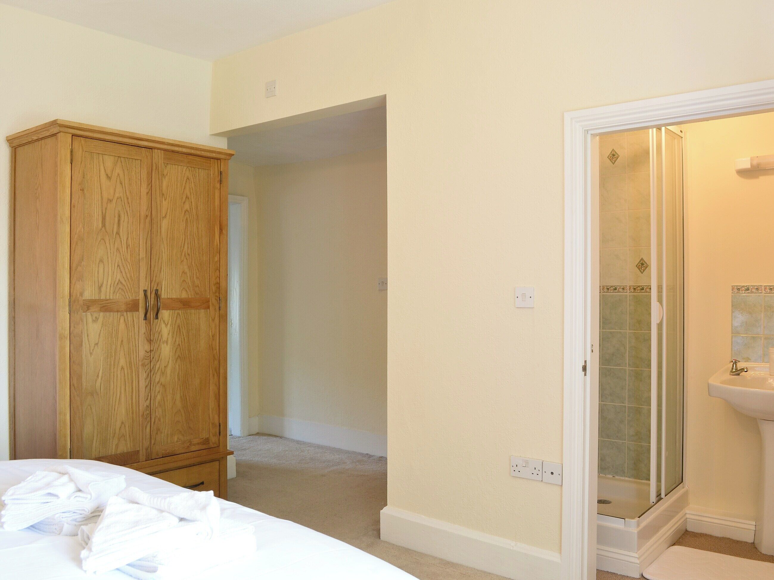 Un dormitorio con un armario de madera, una cama bien hecha y un baño con ducha y lavamanos.