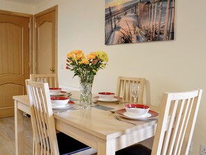Un coin repas avec une table dressée pour quatre personnes, des chaises, un vase de fleurs et un tableau accroché au mur.