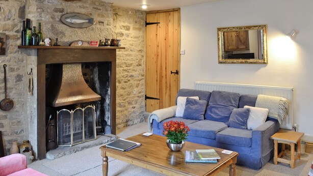 Una sala de estar acogedora con una chimenea de piedra, un sofá azul, una mesa de centro de madera y una mesita auxiliar.