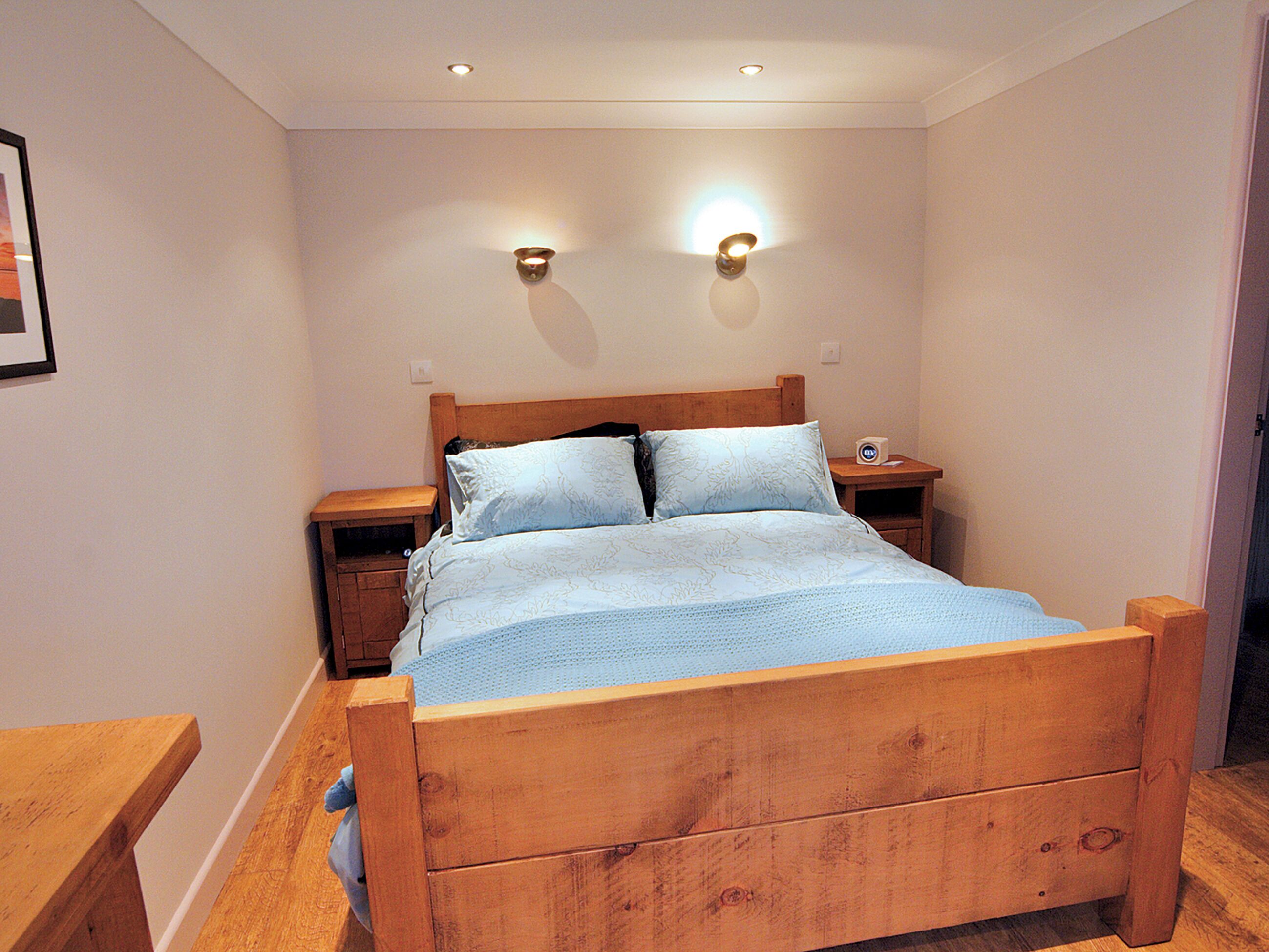 A wooden bed with two nightstands, a wall-mounted light fixture, and a framed picture on the wall.