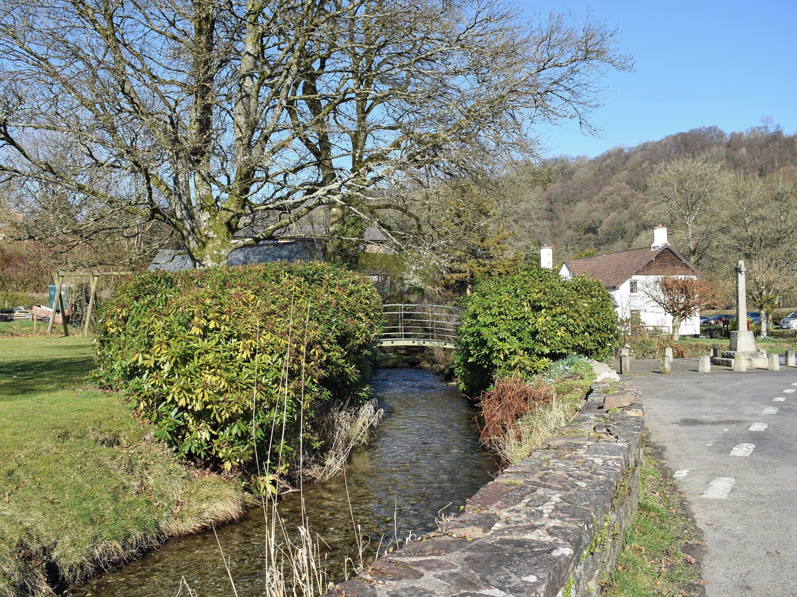 A narrow water channel with a bridge, surrounded by greenery and a stone wall.