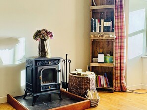 A wood-burning stove, a bookshelf with books, a wicker basket, and a plaid curtain.