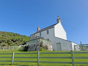 A white building with a stone foundation, a wooden fence, and a hill in the background. - 1 bedroom accommodation in Rispond, near Durness (Rispond, near Durness)