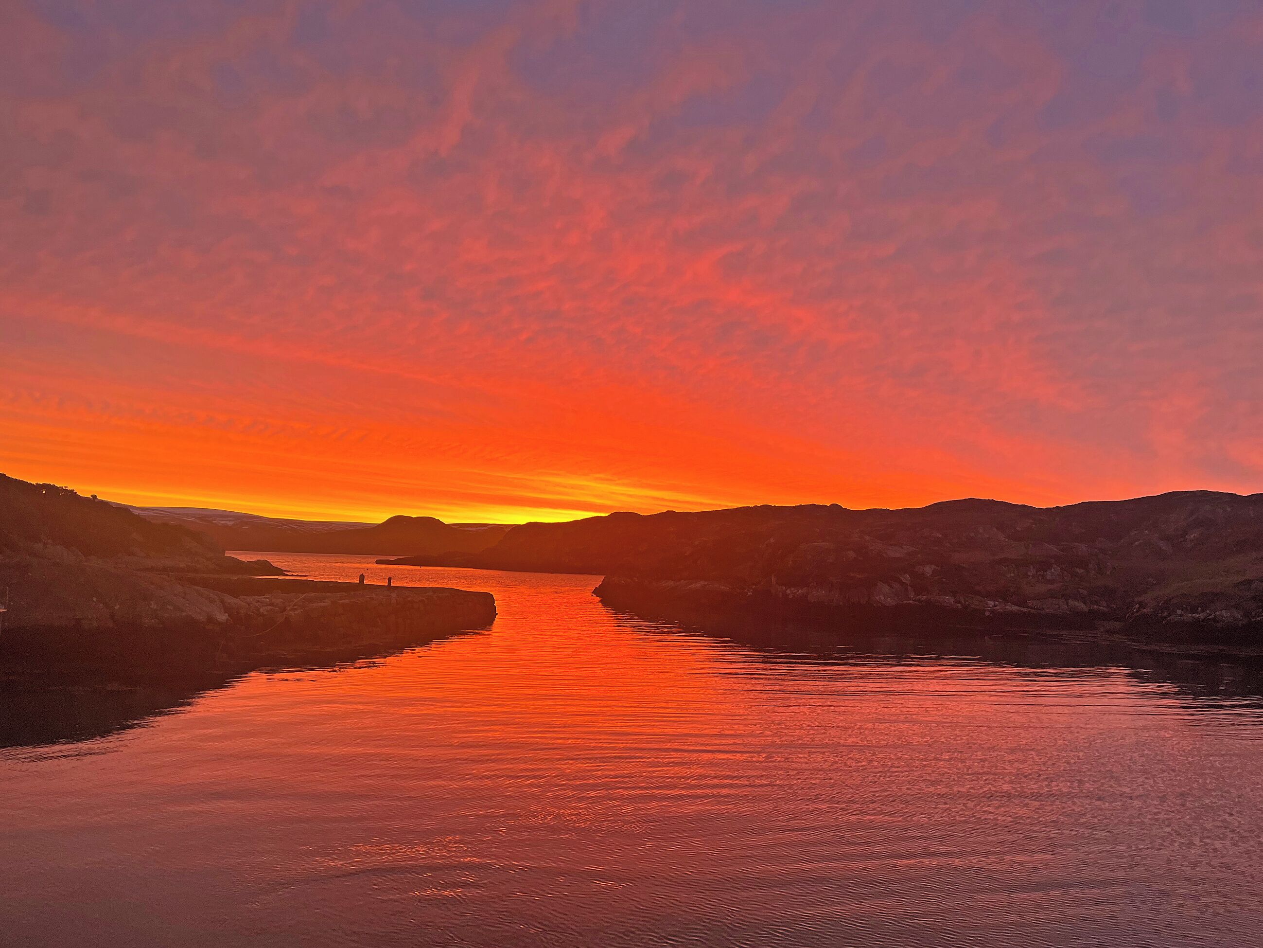 Un coucher de soleil sur une rivière paisible, bordée de collines de chaque côté.