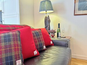 A sofa with red and plaid cushions, a lamp, a bottle of wine, and a glass on a side table. - 1 bedroom accommodation in Rispond, near Durness (Rispond, near Durness)