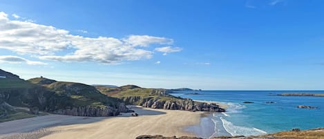 A coastal landscape with a beach, rocky cliffs, and a clear sky.