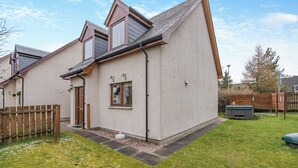 Een huis met twee verdiepingen, een schuin dak, een houten omheining en een kleine tuin.