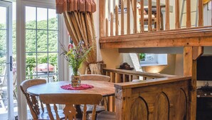 A wooden dining table with chairs, a vase with flowers, and a view of greenery outside. - 2 bedroom accommodation in Polbrock, Washaway (Polbrock, Washaway)