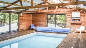 An indoor swimming pool with wooden beams, a blue lounge chair, and a stone wall. - 2 bedroom accommodation in Polbrock, Washaway (Polbrock, Washaway)