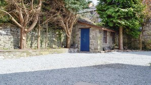 Un bâtiment en pierre avec une porte bleue, entouré de gravier et d’arbres.