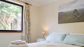 Une chambre à coucher avec un lit, une table de chevet, une lampe, une fenêtre avec des rideaux et un tableau au mur.