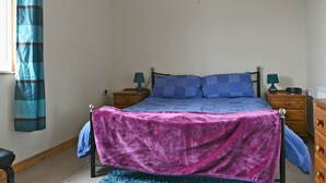 Un dormitorio con una cama, dos mesitas de noche, un ventanal con cortinas y suelo de madera.