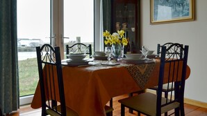 Un comedor con una mesa preparada para cuatro personas, un jarrón de flores amarillas y vistas al exterior a través de amplios ventanales.