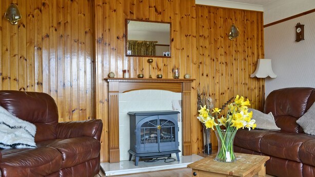 Una sala de estar con dos sofás de cuero, una repisa de madera con chimenea, una mesita de madera y un jarrón de flores.