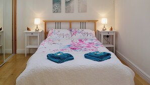 A neatly made bed with floral bedding, two bedside lamps, and a mirror on the left wall. - 1 bedroom accommodation in Capelulo, near Conwy (Capelulo, near Conwy)