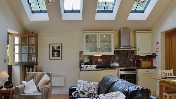 A spacious living area with a leather sofa, a striped armchair, and a glass coffee table. A kitchen with white cabinets and a stove is visible in the background. - 1 bedroom accommodation in Capelulo, near Conwy (Capelulo, near Conwy)