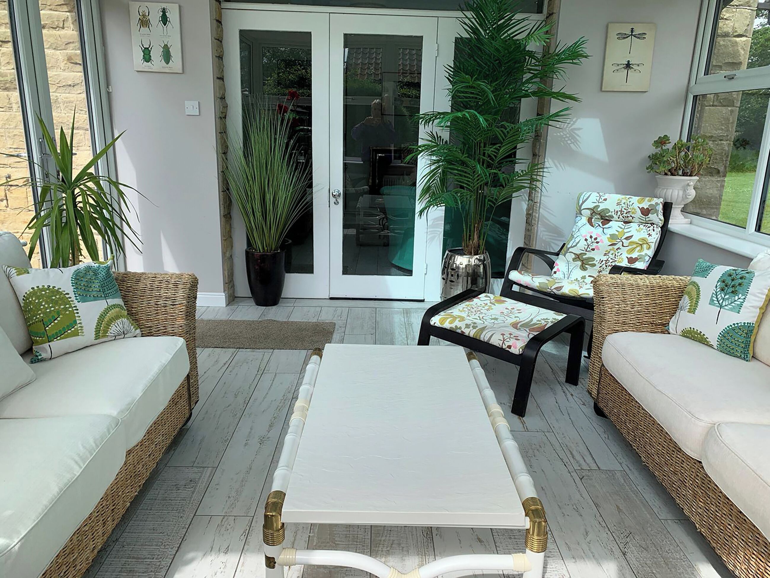 A cozy patio area with wicker furniture, a white table, and potted plants.