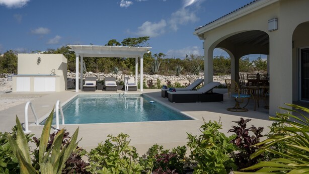 A pool area with lounge chairs, a covered seating area, and a building with a tiled roof.