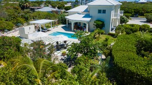 A two-story house with a swimming pool, surrounded by lush greenery and palm trees.