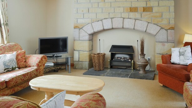 A living room with a stone fireplace, a television, and patterned sofas.