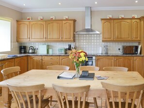 A kitchen with wooden cabinets, a stainless steel range hood, a dining table with chairs, and a vase with flowers.