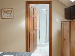 Une pièce comprenant un lit, une armoire en bois, un téléviseur posé sur le dessus, un tableau encadré accroché au mur et un espace douche visible à travers une porte ouverte.