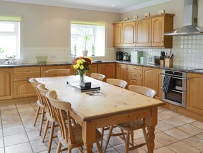 Une cuisine avec des meubles de rangement en bois, une table à manger avec des chaises, une cuisinière et une fenêtre avec des stores.