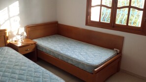Ein kleines Zimmer mit einem Einzelbett, einem hölzernen Kopfteil, einem Nachttisch mit Lampe und einem Fenster mit Blick ins Grüne.