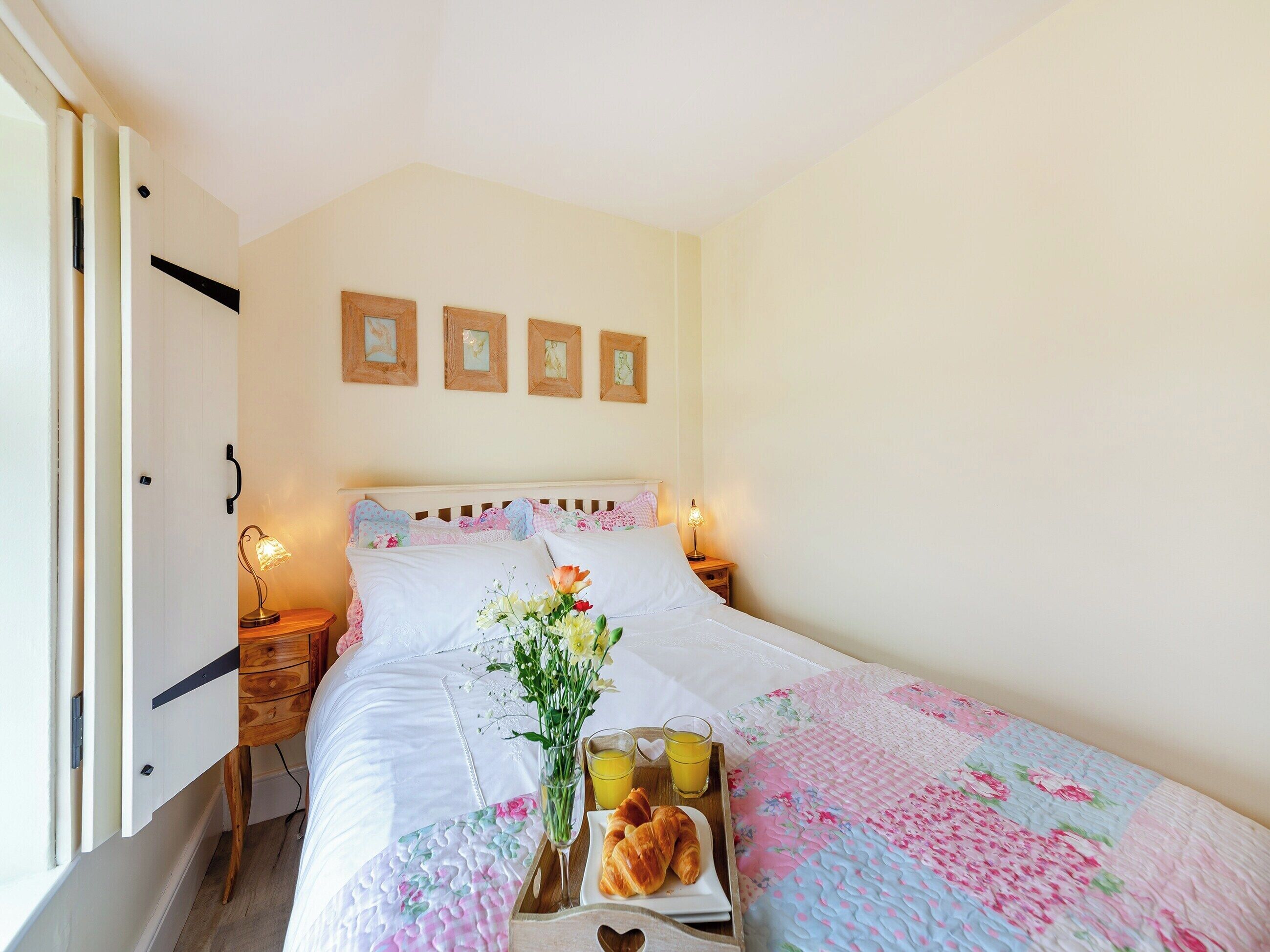 A neatly made bed with a floral quilt, a bedside table with a lamp, and a tray with croissants and orange juice.