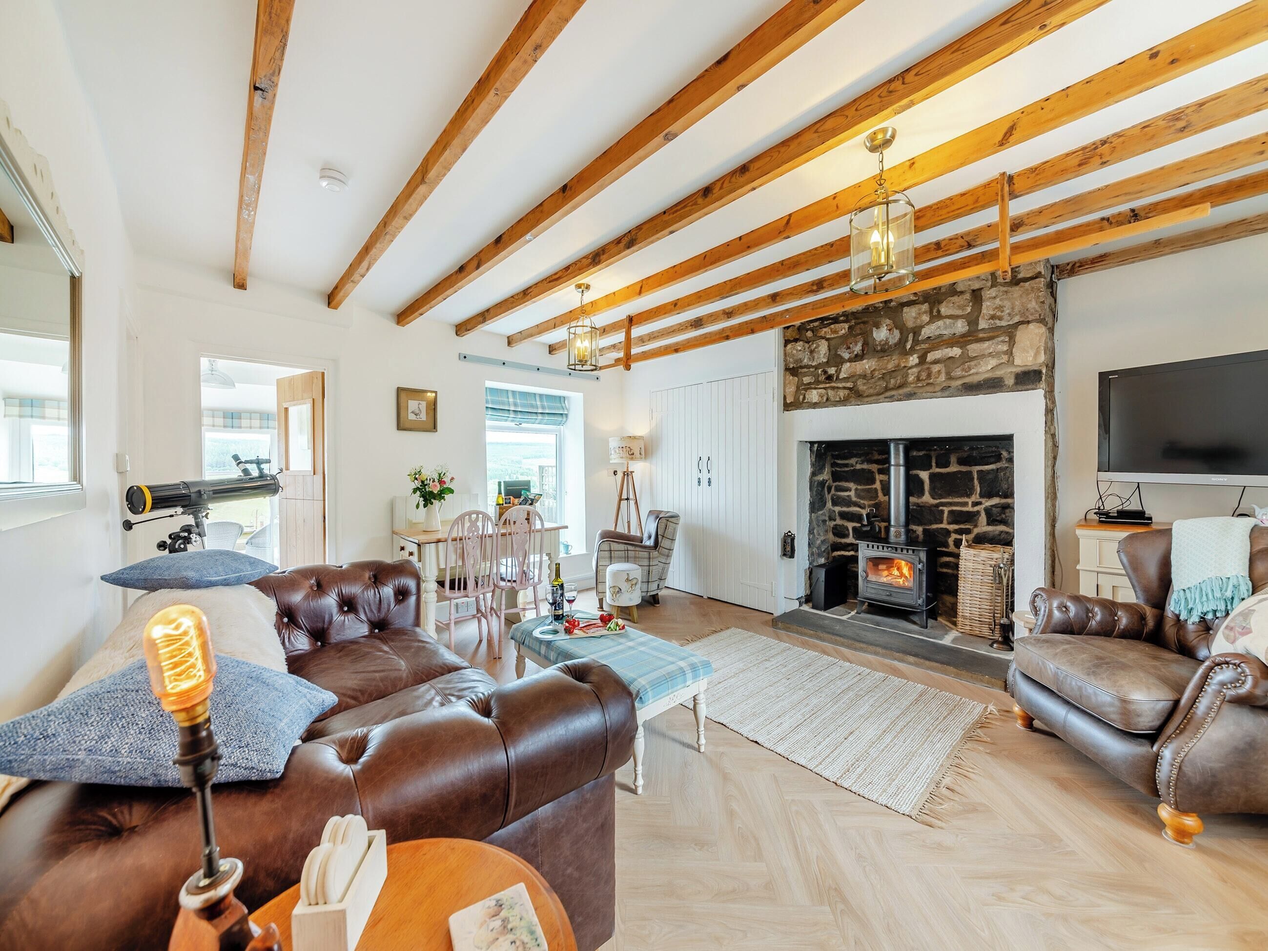 Una sala acogedora con chimenea de piedra, sofás de cuero, vigas de madera y un televisor.