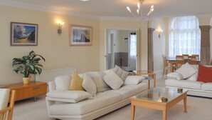 A living room with a sofa, coffee table, and a dining area with chairs. - 2 bedroom accommodation in Tehidy Park, near Camborne (Tehidy Park, near Camborne)