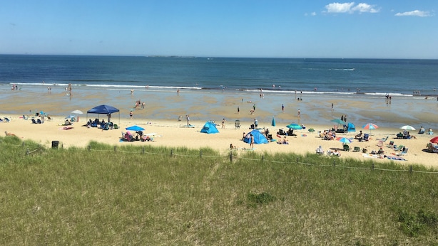 Una playa con tiendas de campaña y sombrillas, gente tomando el sol y el océano al fondo.