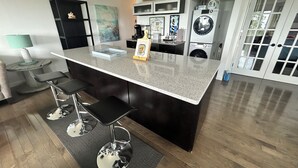 Una cocina moderna con una isla central, taburetes de bar, una cafetera y una lavadora.