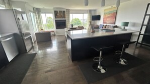Cocina moderna con isla central, taburetes de bar, zona de comedor con sofá y un ventanal con cortinas.