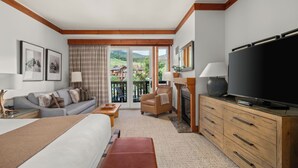Una habitación de hotel con cama, sofá, televisor, chimenea y balcón con vistas panorámicas.