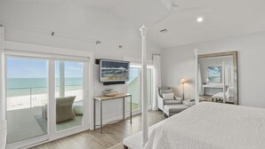 A bedroom with a large bed, a TV, a balcony with a view of the beach, and a ceiling fan. - Graceland: Stunning Views, Screened Porch, End of North Cape! (Cape San Blas)