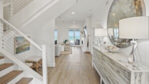 A spacious hallway with a wooden staircase, a marble countertop, and a large mirror. - Graceland: Stunning Views, Screened Porch, End of North Cape! (Cape San Blas)