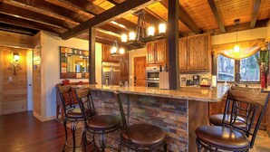 Una cocina rústica con vigas de madera a la vista, una isla de piedra con taburetes de bar y un ventanal con vistas al exterior.