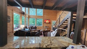 Un interior de cabaña con encimera de piedra, paredes de madera, chimenea y una escalera.