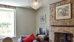 A cozy living room with a stone fireplace, a television on a wooden table, and a comfortable armchair with a red pillow. - 3 bedroom accommodation in Llandybie, near Llandeilo (Llandybie, near Llandeilo)