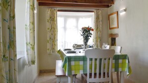 A dining area with a table set for two, a bench, and a window with curtains. - 3 bedroom accommodation in Llandybie, near Llandeilo (Llandybie, near Llandeilo)