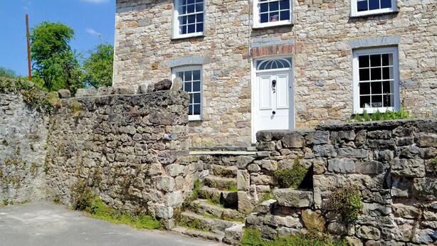 A stone building with multiple windows and a door, featuring a stone wall and a small garden area. - 3 bedroom accommodation in Llandybie, near Llandeilo (Llandybie, near Llandeilo)