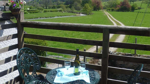 Ein Balkon mit Tisch für Zwei, einer Weinflasche und einem Blumenkorb.