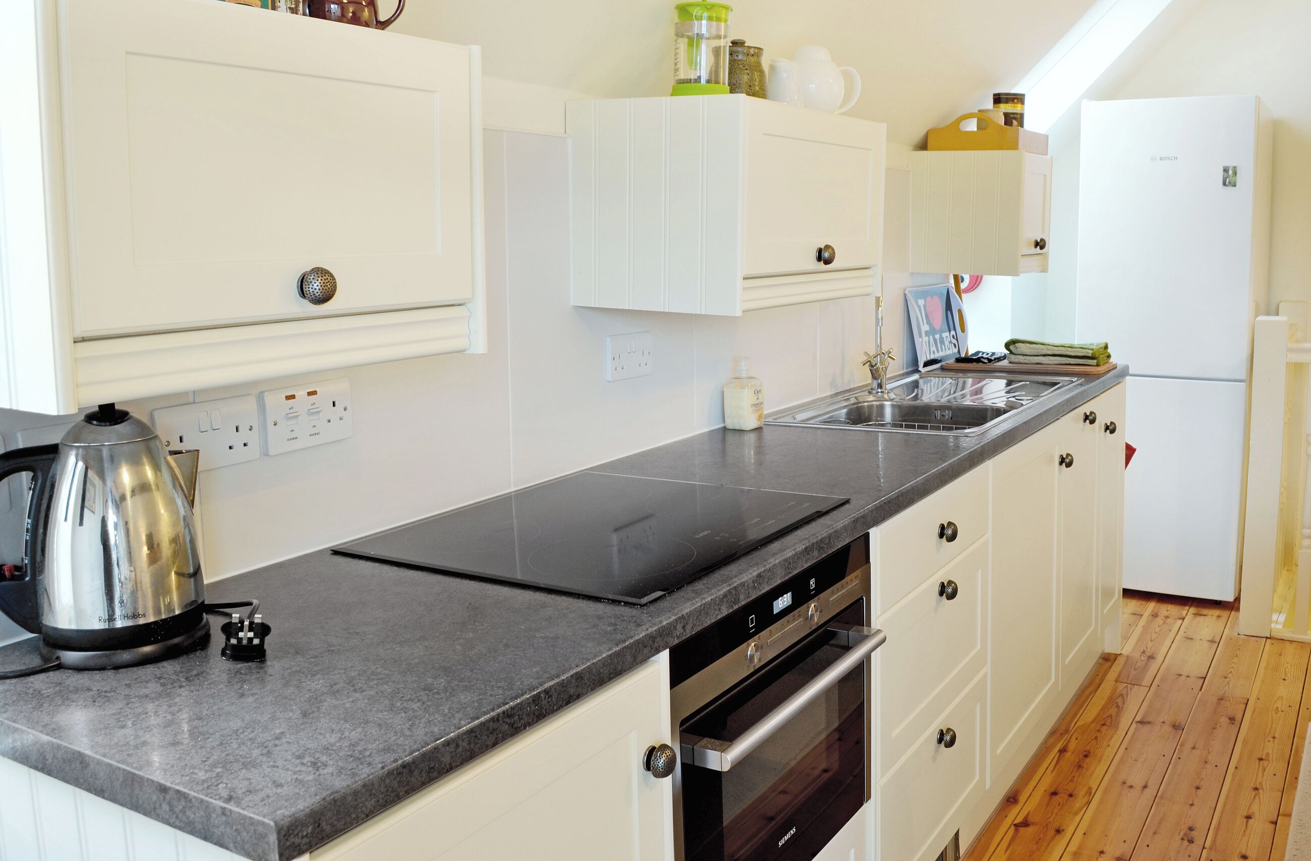 A modern kitchen with a built-in oven, a dishwasher, and a countertop with a kettle.