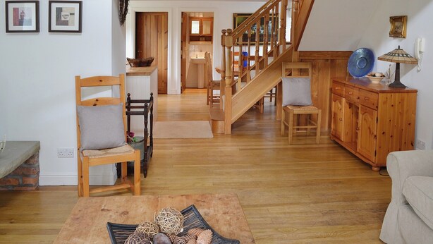 A spacious living room with a wooden staircase, a dining area, and a kitchen in the background. - Wee Bridge Farm Cottage (Mobberley, near Knutsford)