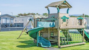 Ein Spielplatz mit Rutsche, Kletternetz und einer Holzspielhütte.
