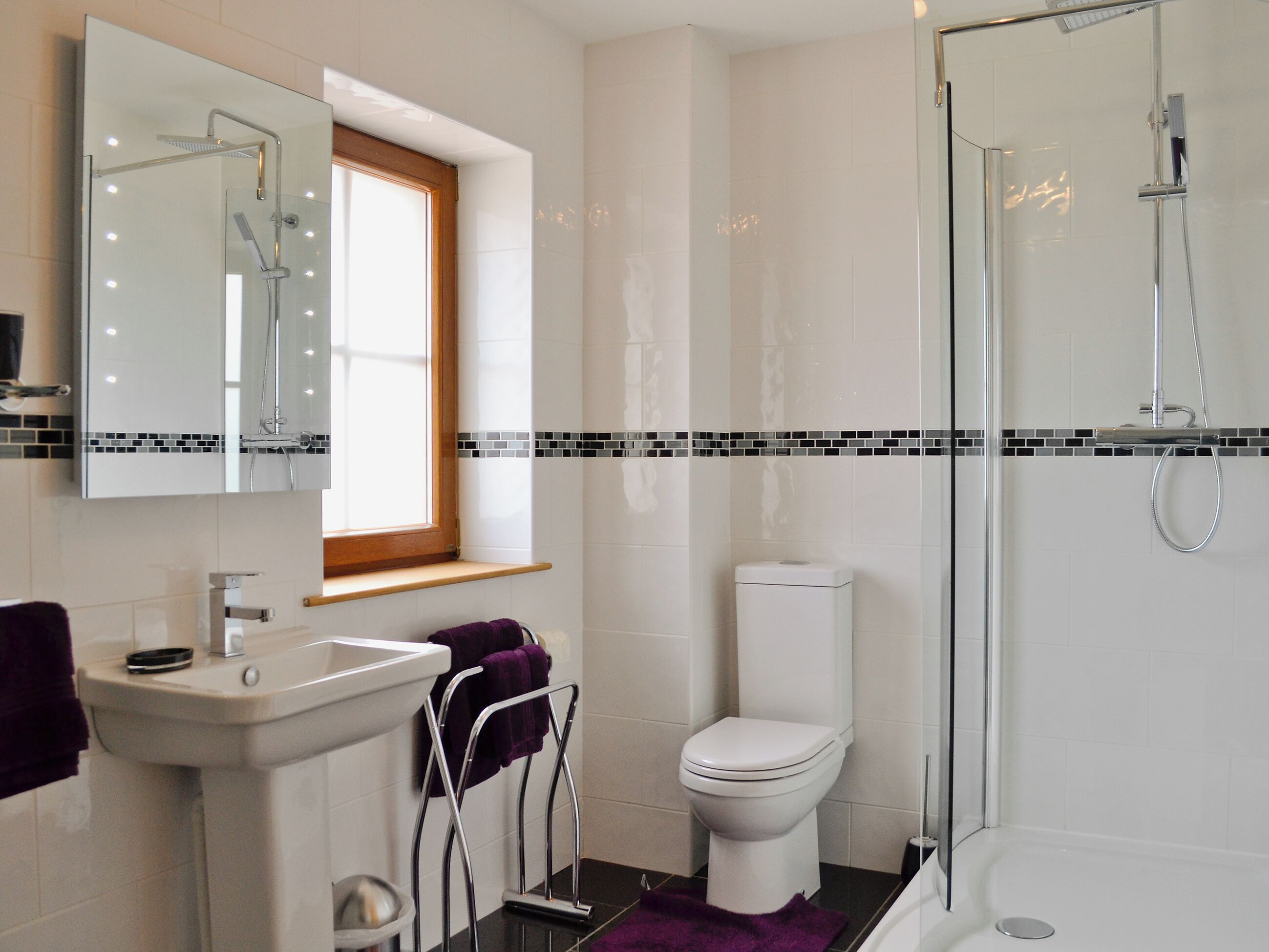 Een moderne badkamer met een douchecabine van glas, een wit toilet en een wastafel met spiegel.
